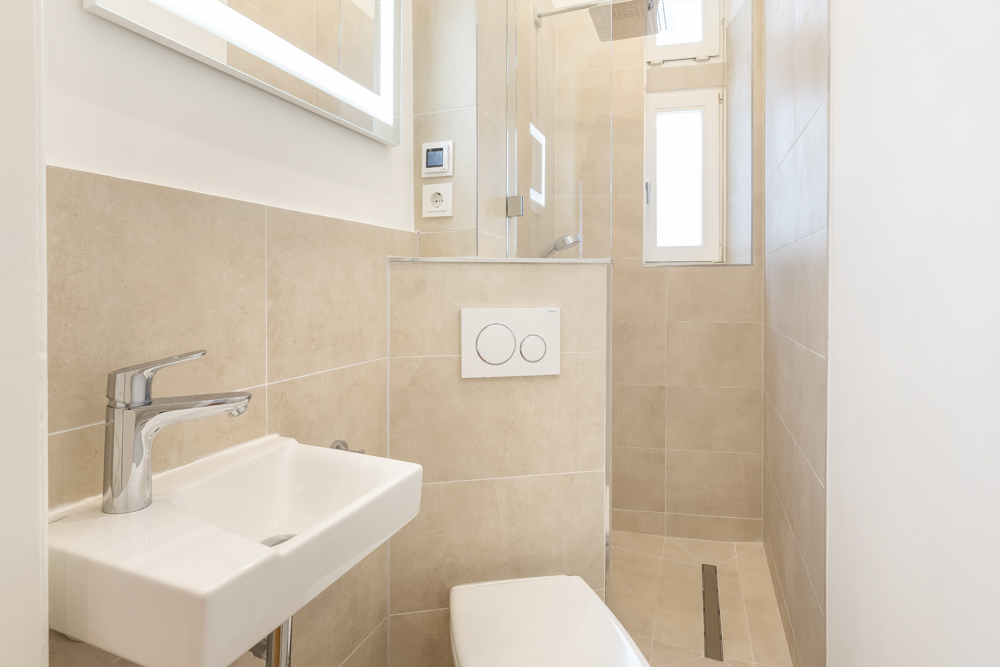 Modernes, kleines Badezimmer mit Dusche, WC, Waschbecken und Fenster, beige gefliest.