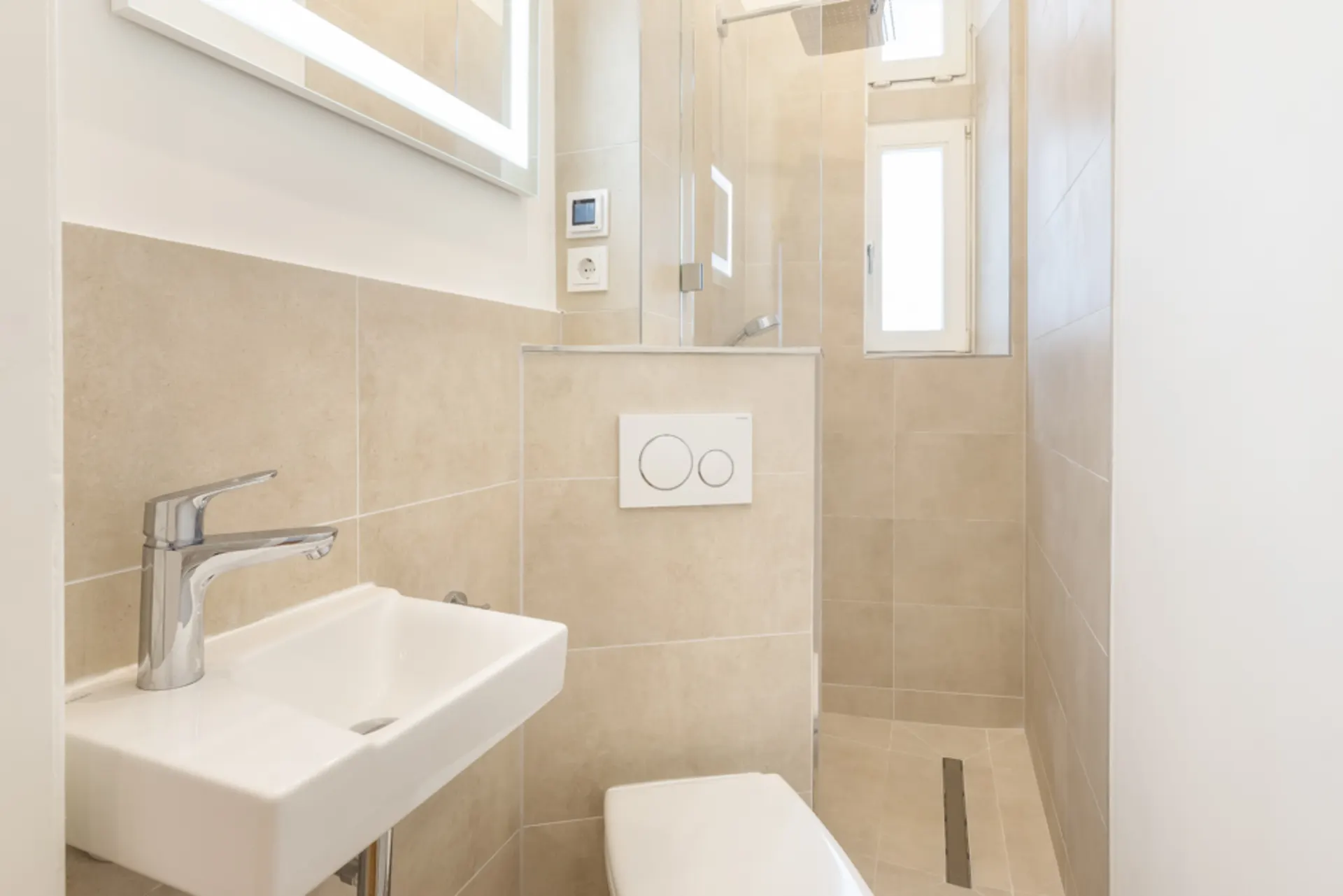 Modernes, kleines Badezimmer mit Dusche, WC, Waschbecken und Fenster, beige gefliest.