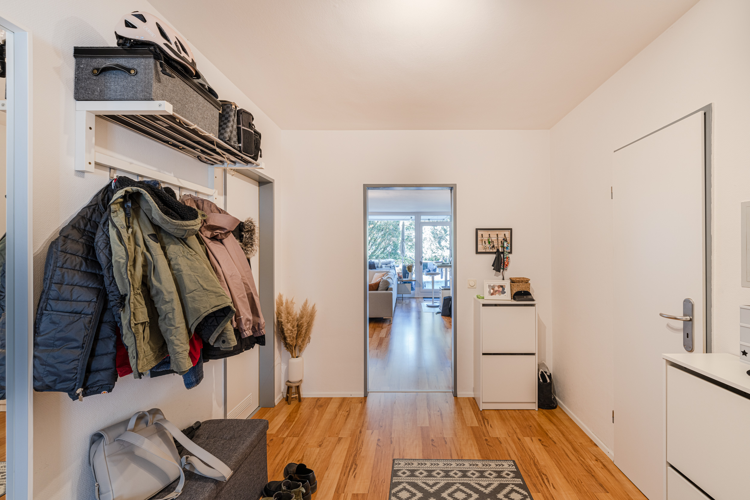 Heller Flur mit Holzboden, Garderobe, Schuhen, Kommoden und Blick ins Wohnzimmer.