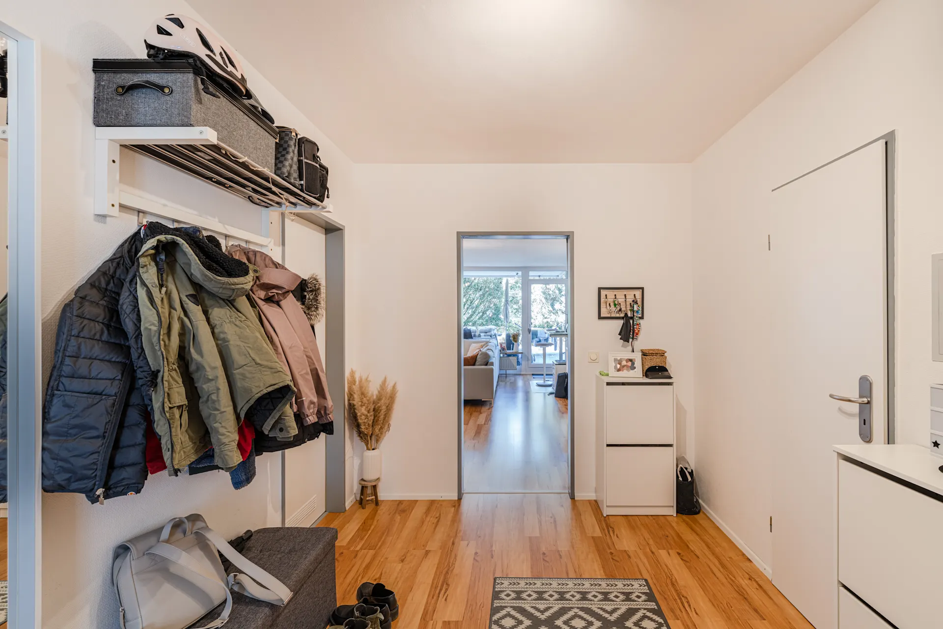 Heller Flur mit Holzboden, Garderobe, Schuhen, Kommoden und Blick ins Wohnzimmer.