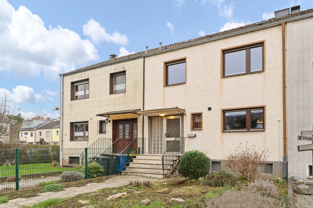 Vorderansicht eines zweistöckigen Reihenhauses mit Vorgarten und Treppe zum Eingang.