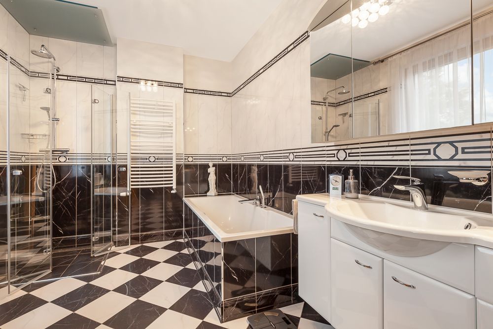Modernes Badezimmer mit schwarz-weißem Fliesenboden, Badewanne, Dusche und großem Spiegel.