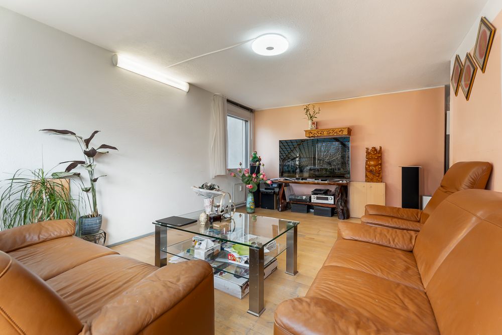 Wohnzimmer mit braunen Ledersofas, Glastisch, Fernseher, Pflanzen und Holzboden.
