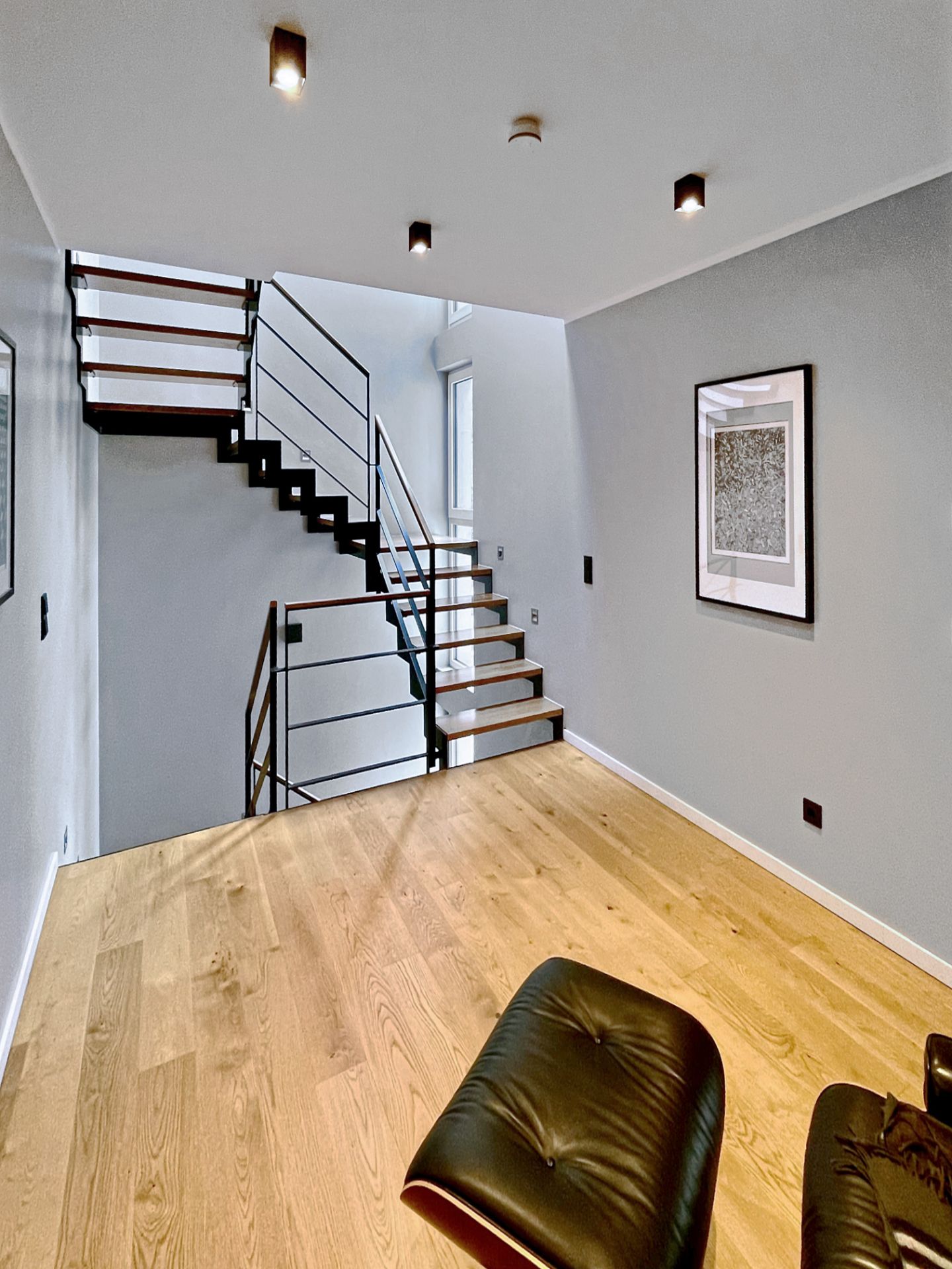 Modernes Zimmer mit Holzfußboden, Treppe mit Metallgeländer und Wandbild.