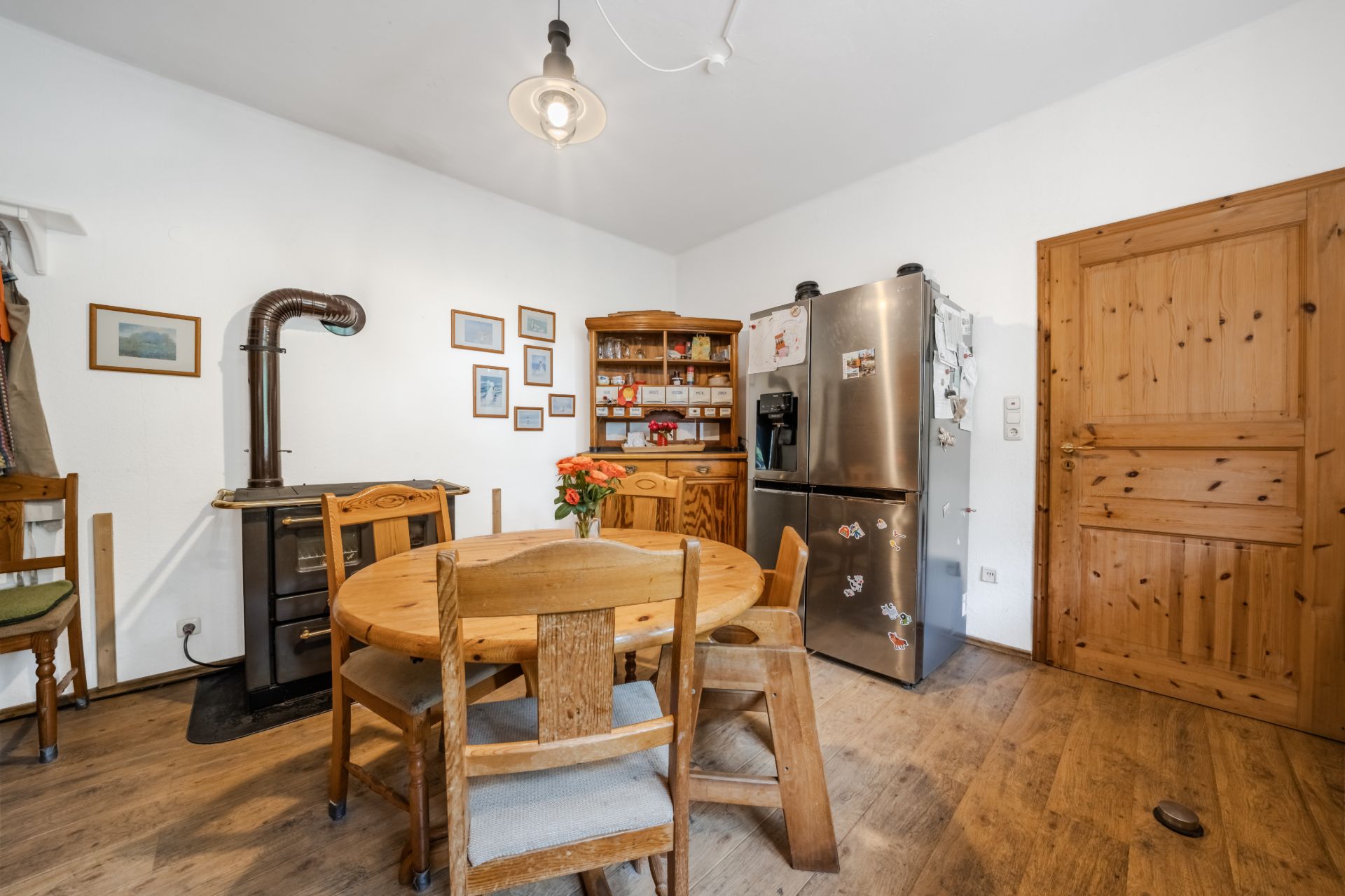 Küche mit Holztisch, Stühlen, Holzofen, großem Kühlschrank und Holzschrank auf Holzboden.