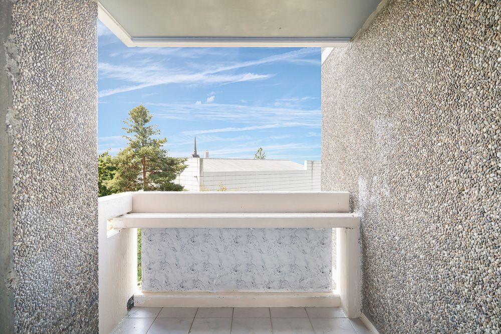Kleiner Balkon mit rau verputzten Wänden und Blick auf Bäume und Himmel.