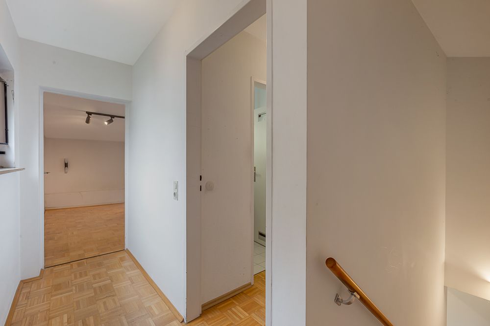 Flur mit Parkettboden, Zugang zu Zimmern und Treppe mit Holzhandlauf.