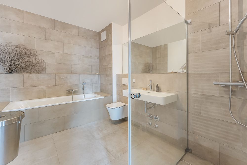 Modernes Badezimmer mit Badewanne, Dusche, Waschbecken und Toilette, alles in beigen Fliesen.
