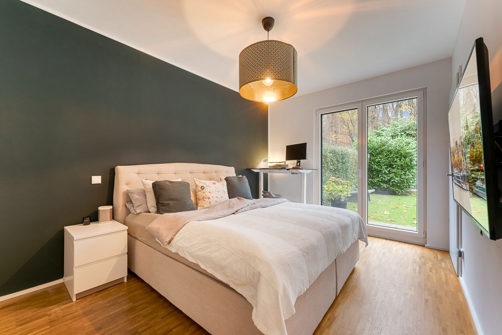 Helles Schlafzimmer mit Doppelbett, Schreibtisch, Nachttisch und Zugang zum Garten durch große Glas­türen.