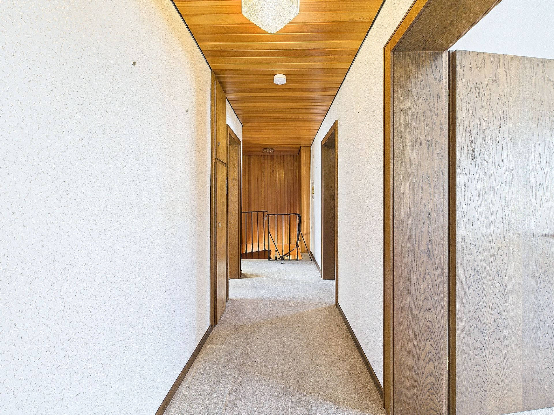 Heller Flur mit Holztüren, Holzdecke und Teppichboden in einem Wohnhaus.