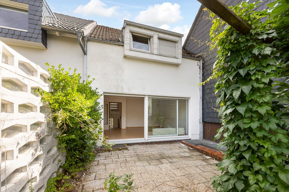 Gepflasterter Innenhof mit Pflanzen, großer Glasschiebetür und Fenster eines Wohnhauses.