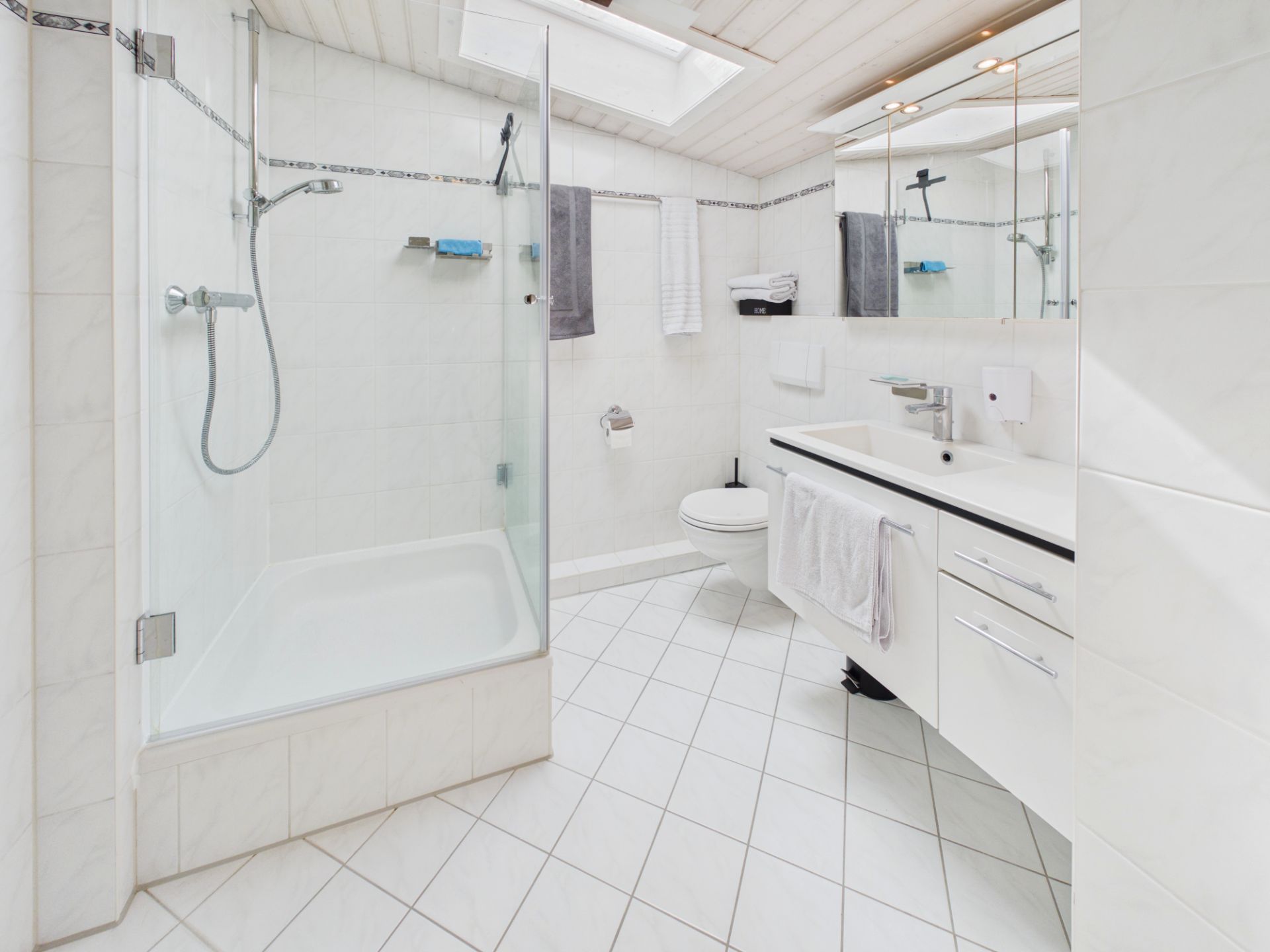 Helles Badezimmer mit Dusche, Waschbecken, Toilette und großem Spiegel.