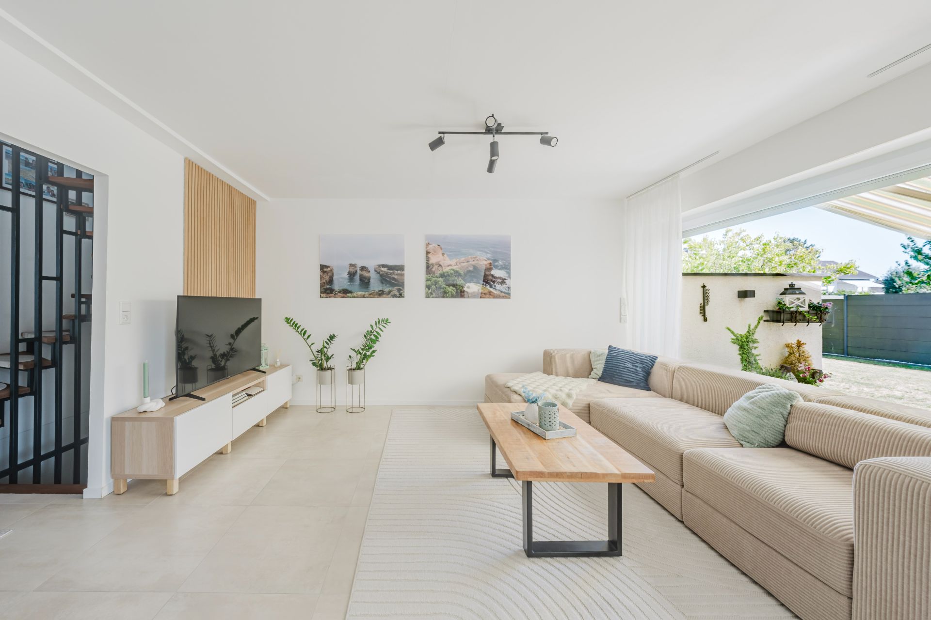 Helles Wohnzimmer mit großer Eckcouch, Couchtisch, Fernseher und Zugang zur Terrasse.