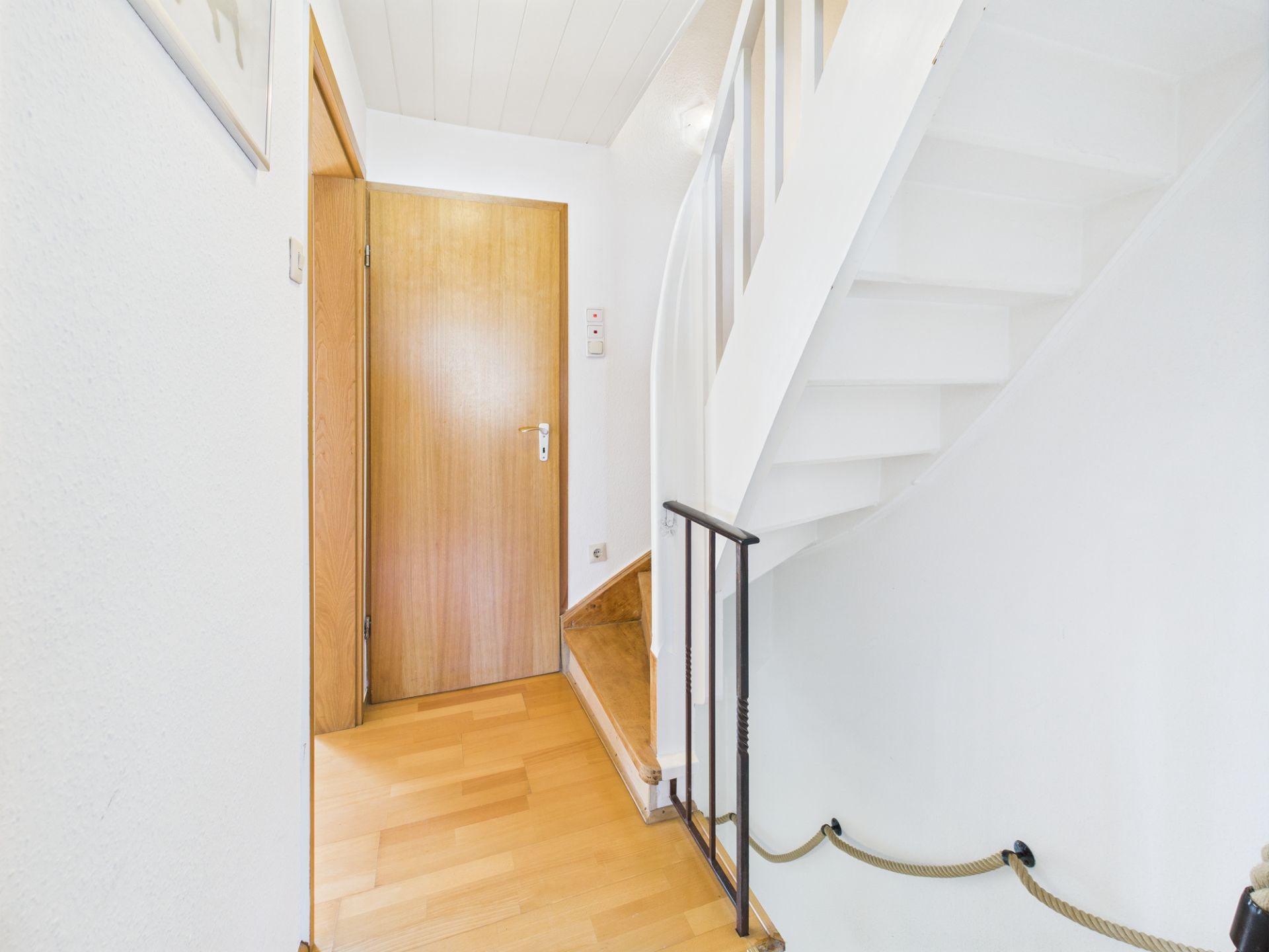 Heller Flur mit Holzfußboden, Holztür und weißer Treppe nach oben.