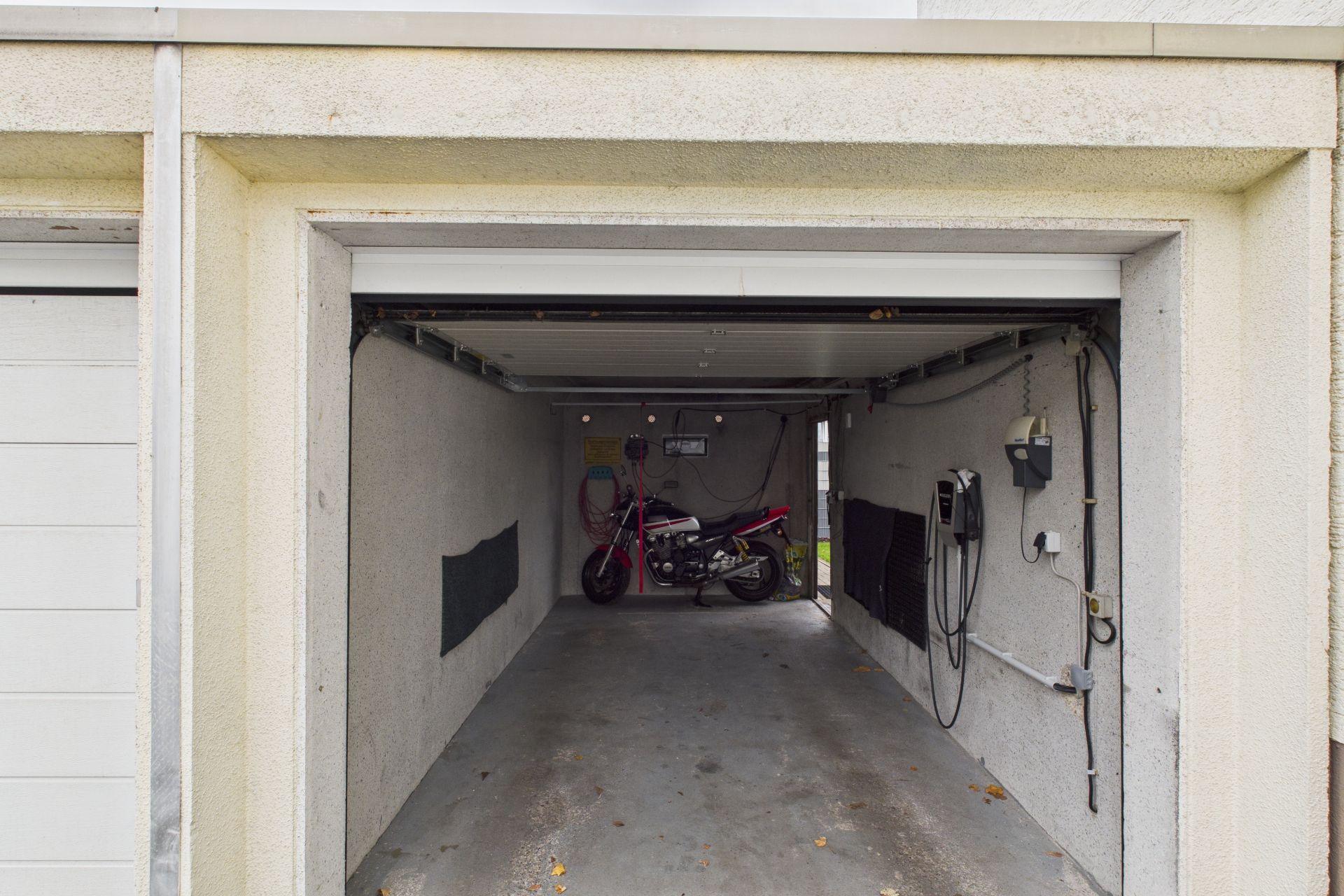 Offene Garagenansicht mit einem Motorrad und Kabeln an den Wänden.