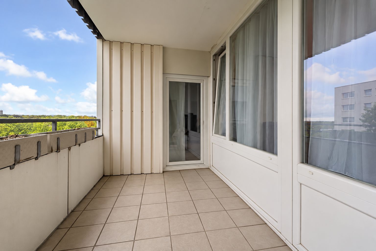 Überdachter Balkon mit Fliesenboden und Glasgeländer, angrenzend an große Fensterfront.