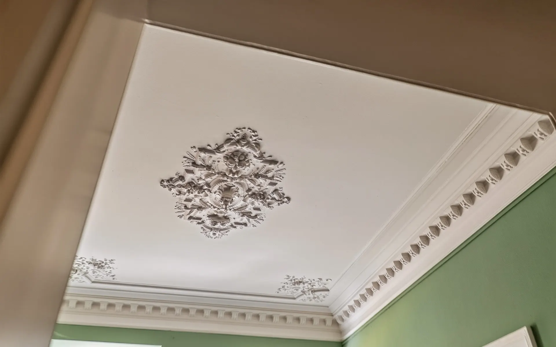 Weiße Stuckdecke mit Verzierungen und grün gestrichenen Wänden im Wohnraum.