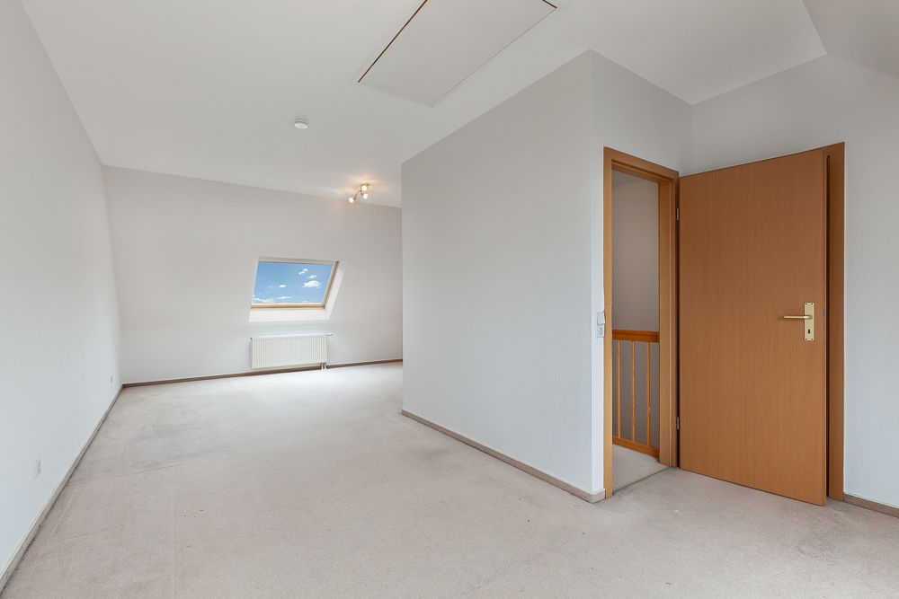 Heller, leerer Raum mit Dachfenster, weiß gestrichenen Wänden und geöffneter Holztür.