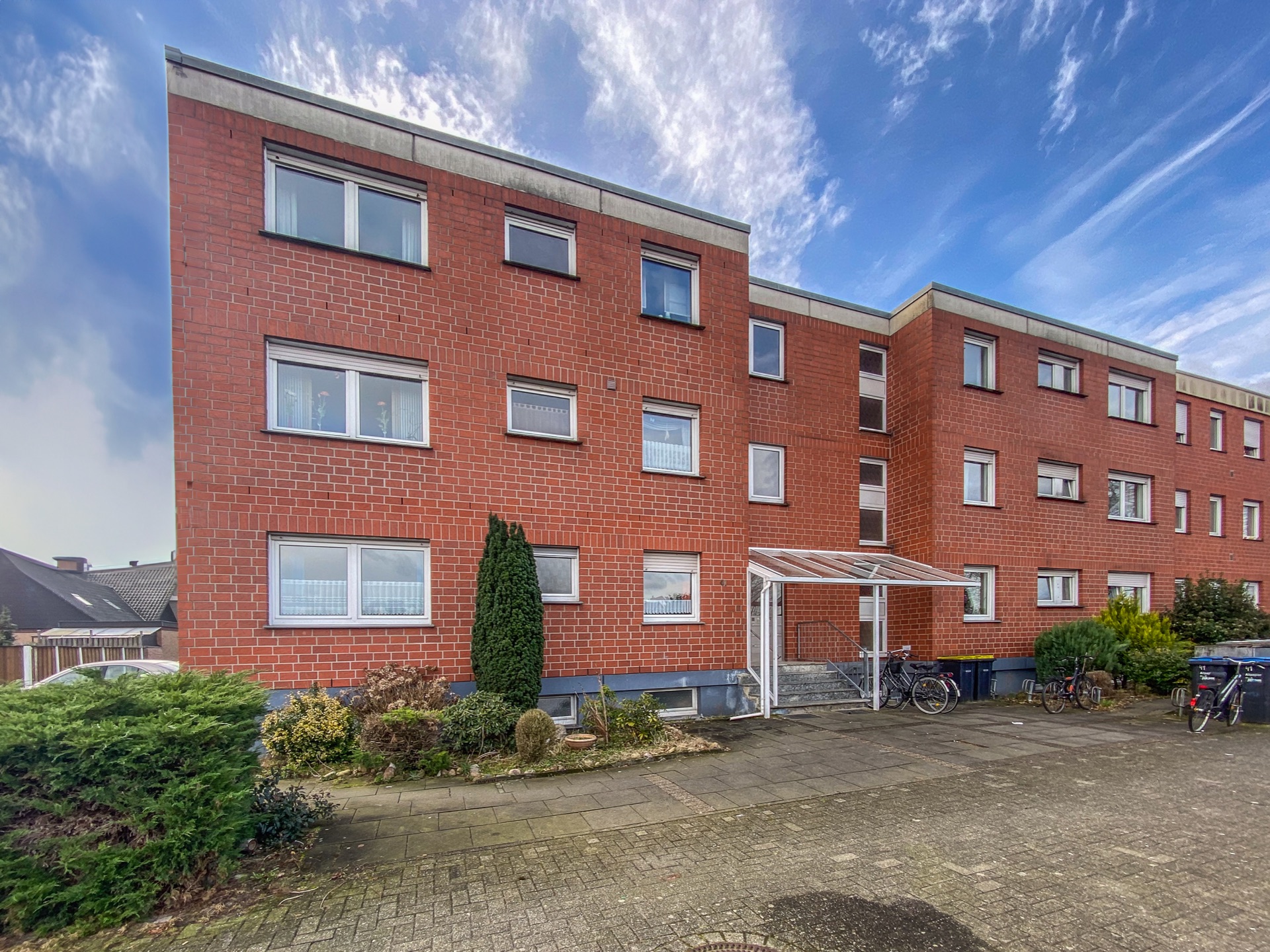 Dreistöckiges Wohnhaus aus rotem Klinker mit mehreren Fenstern und einem überdachten Eingang.