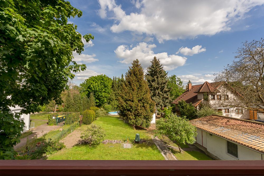 Blick auf einen großen, grünen Garten mit Bäumen und angrenzenden Wohnhäusern.