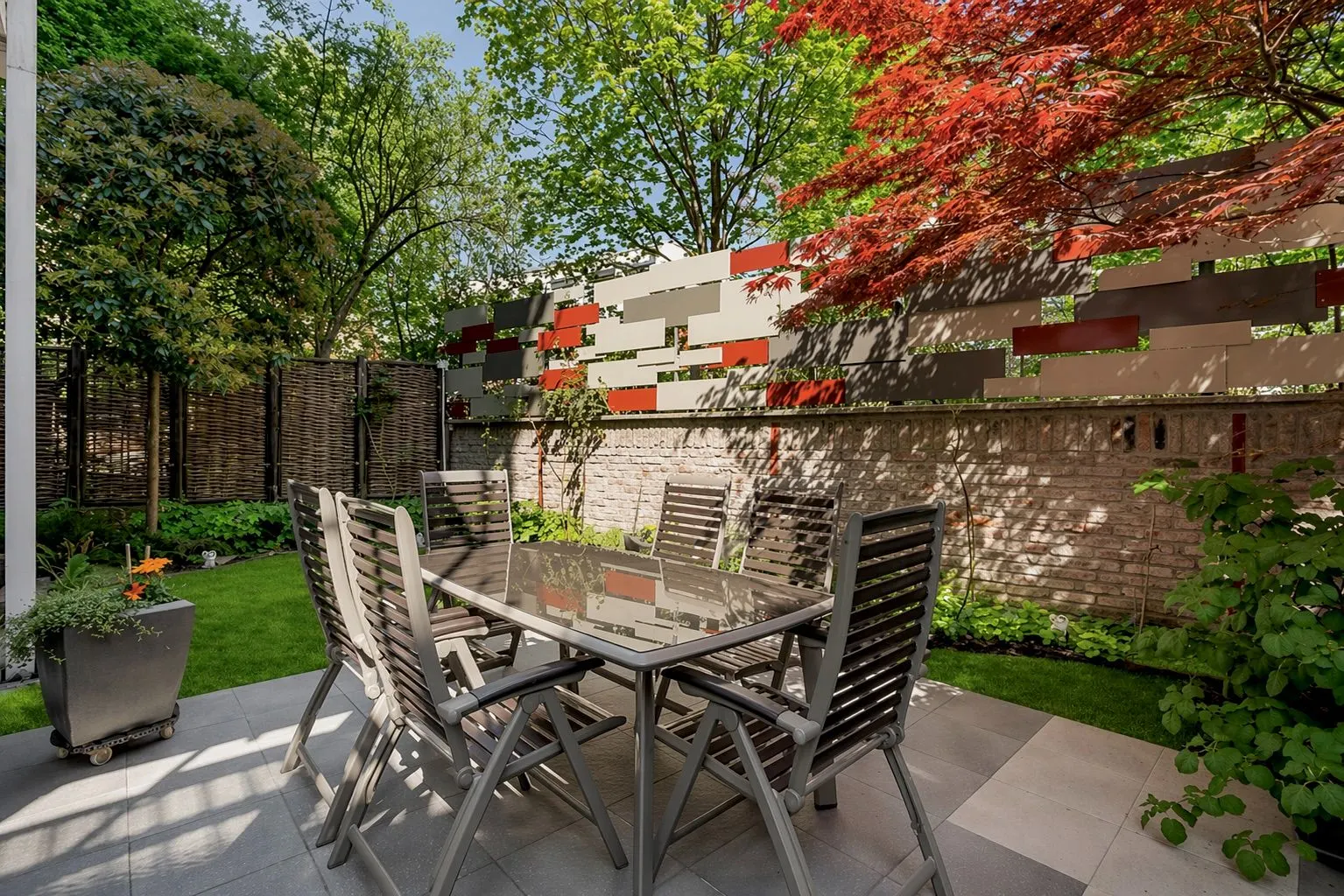 Moderner Garten mit Tisch, Stühlen, Pflanzen und dekorativem Zaun auf einer Terrasse.