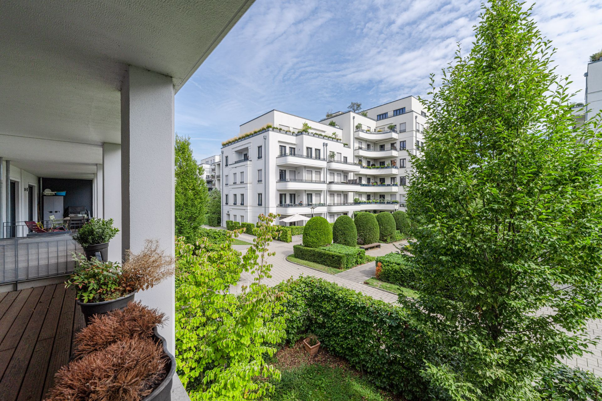 Blick von einem Balkon auf gepflegte Wohnanlagen mit Bäumen und grünen Hecken.
