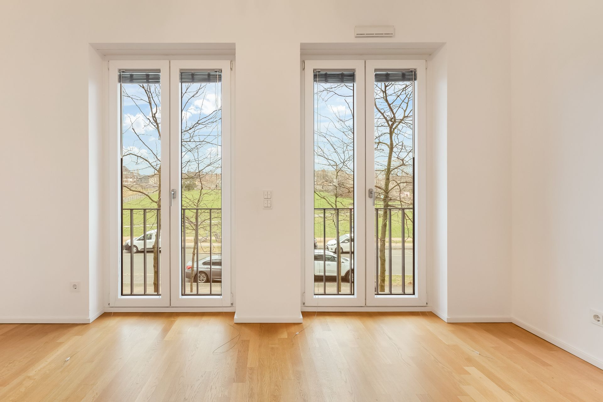 Helles Zimmer mit zwei großen Fenstertüren und Parkettboden, Blick ins Grüne.