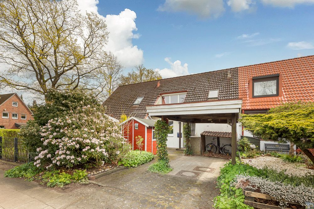 Einfamilienhaus mit rotem Dach, Carport, Vorgarten und blühenden Büschen, Fahrrad unter dem Carport.