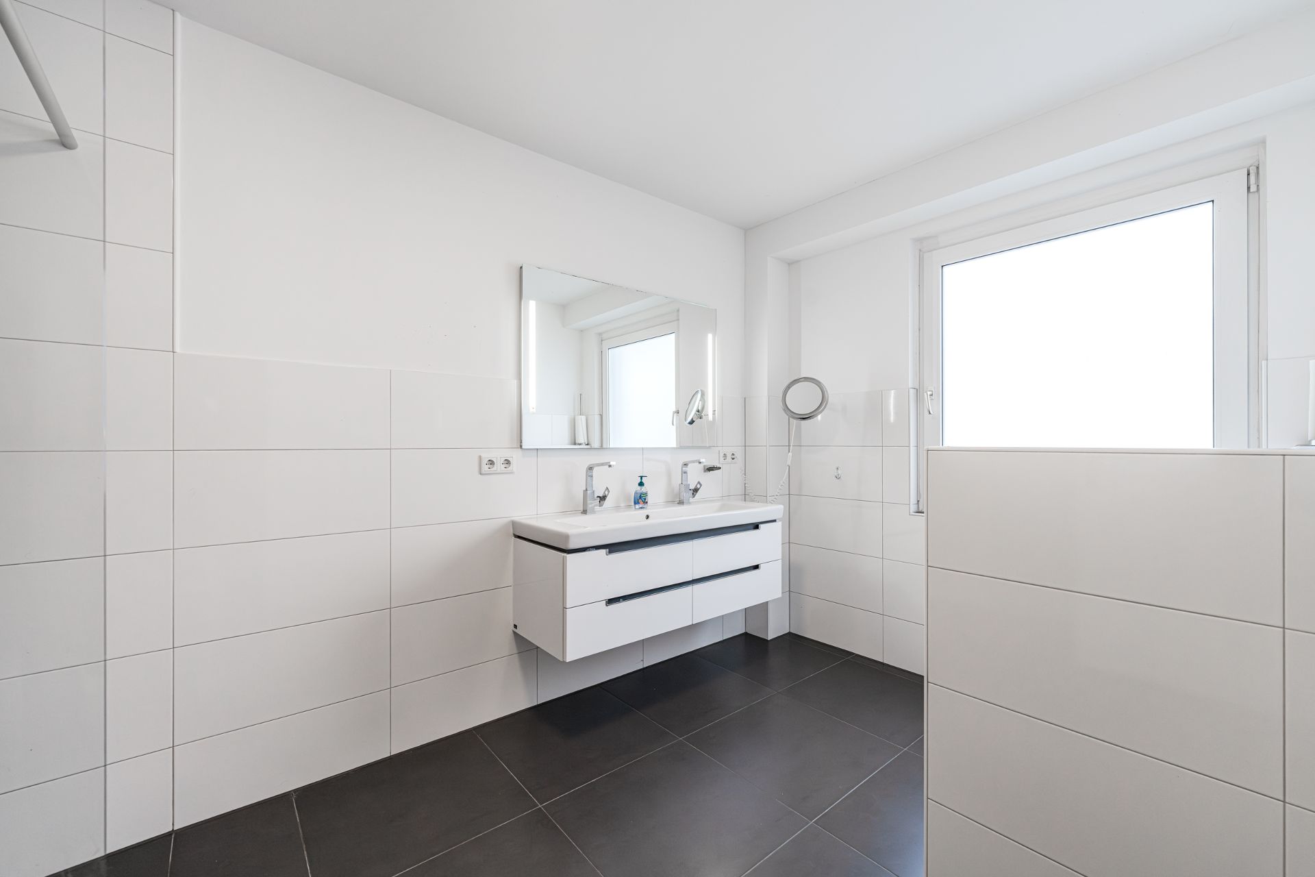 Modernes Badezimmer mit weißem Doppelwaschtisch, großem Spiegel und Fenster.