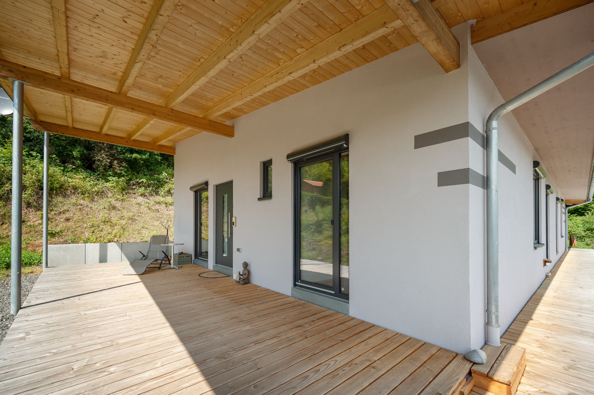Überdachte Holzterrasse mit Zugang zu einem modernen weißen Wohnhaus.