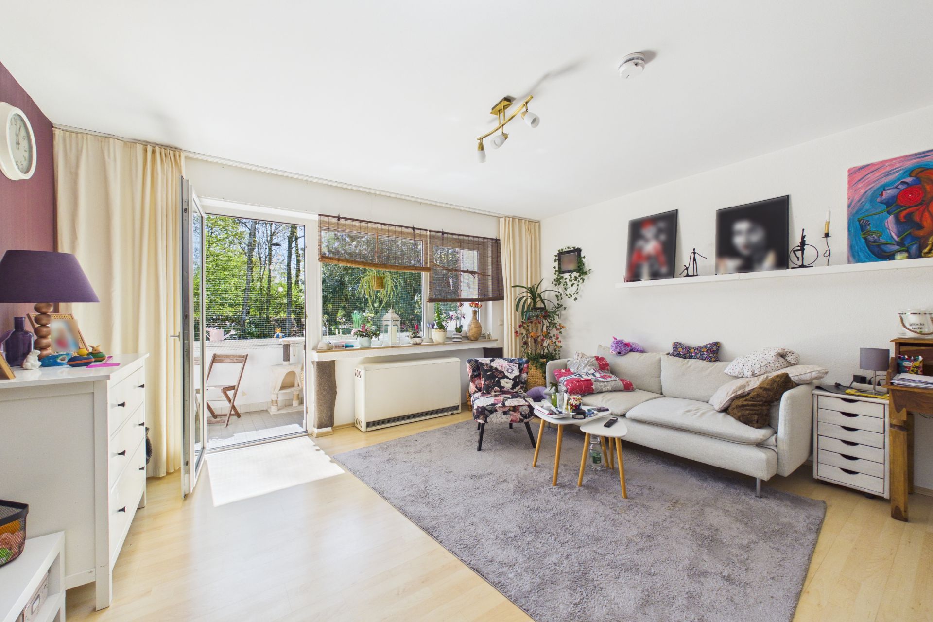 Helles Wohnzimmer mit Sofa, Sessel, Teppich und Zugang zum Balkon.