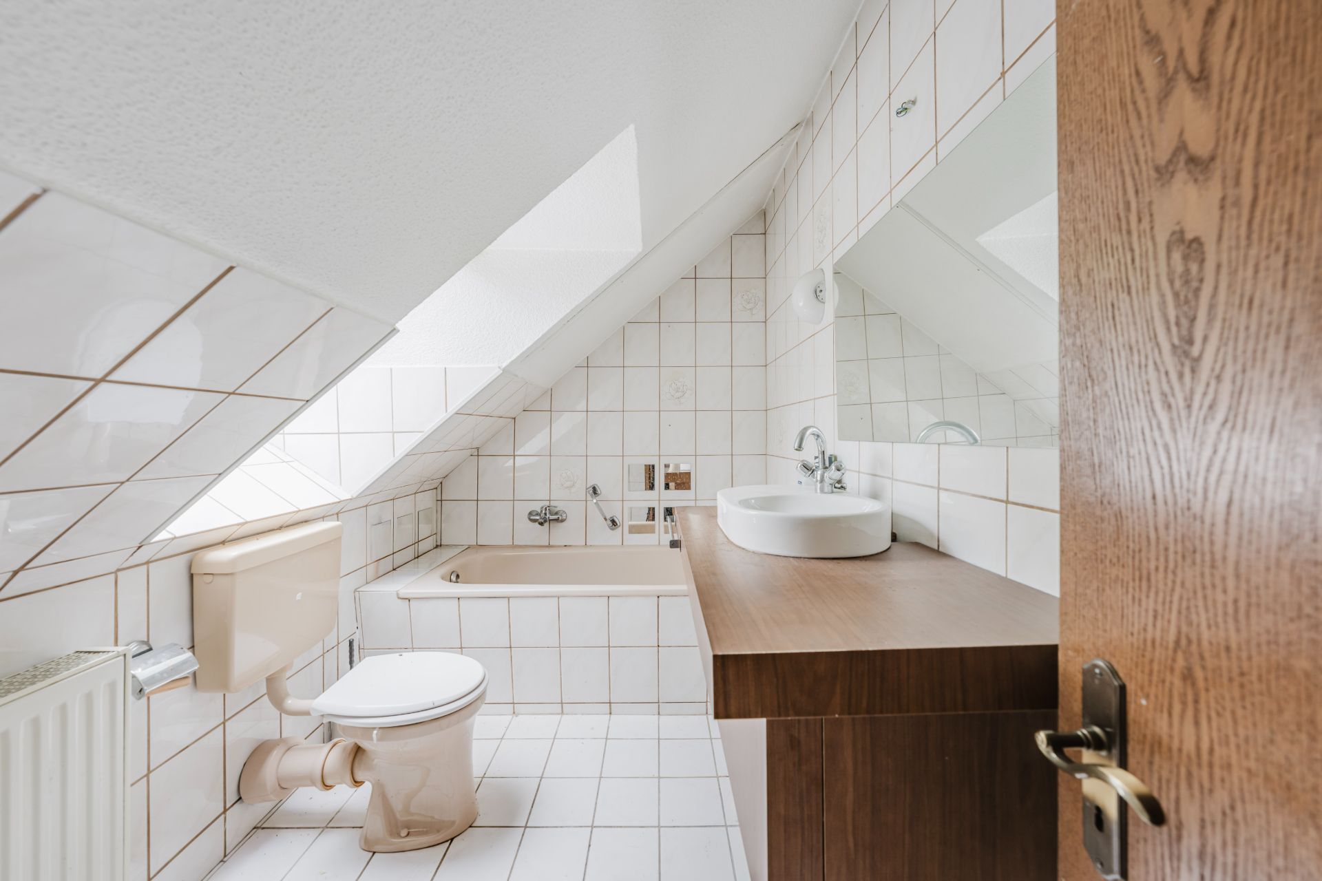 Helles Badezimmer mit Dachschräge, Badewanne, Toilette und Waschtisch mit Spiegel.