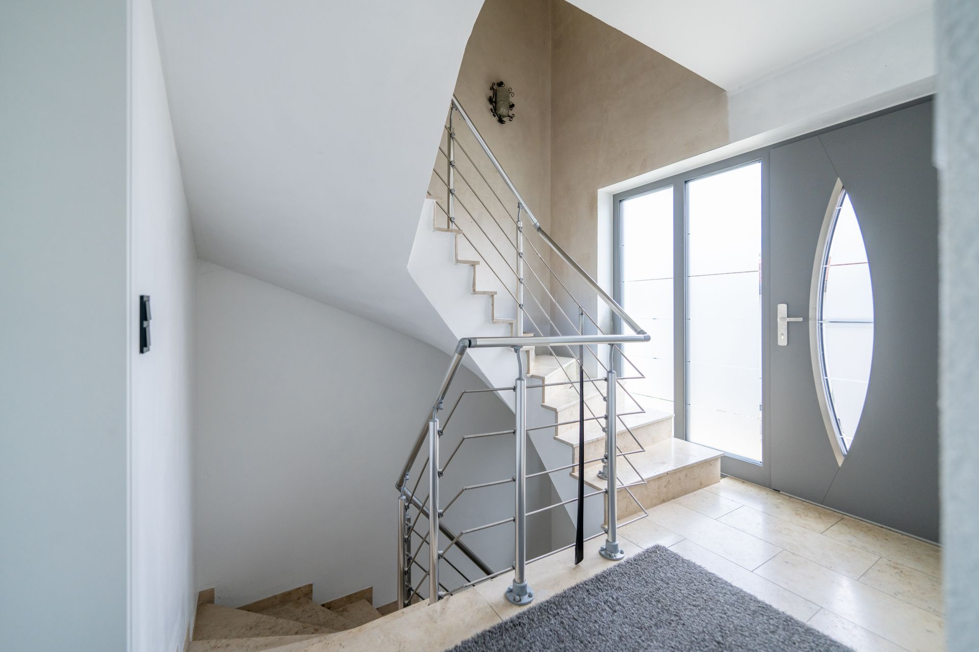 Moderne Eingangshalle mit Treppe, Metallgeländer und großer Glastür.