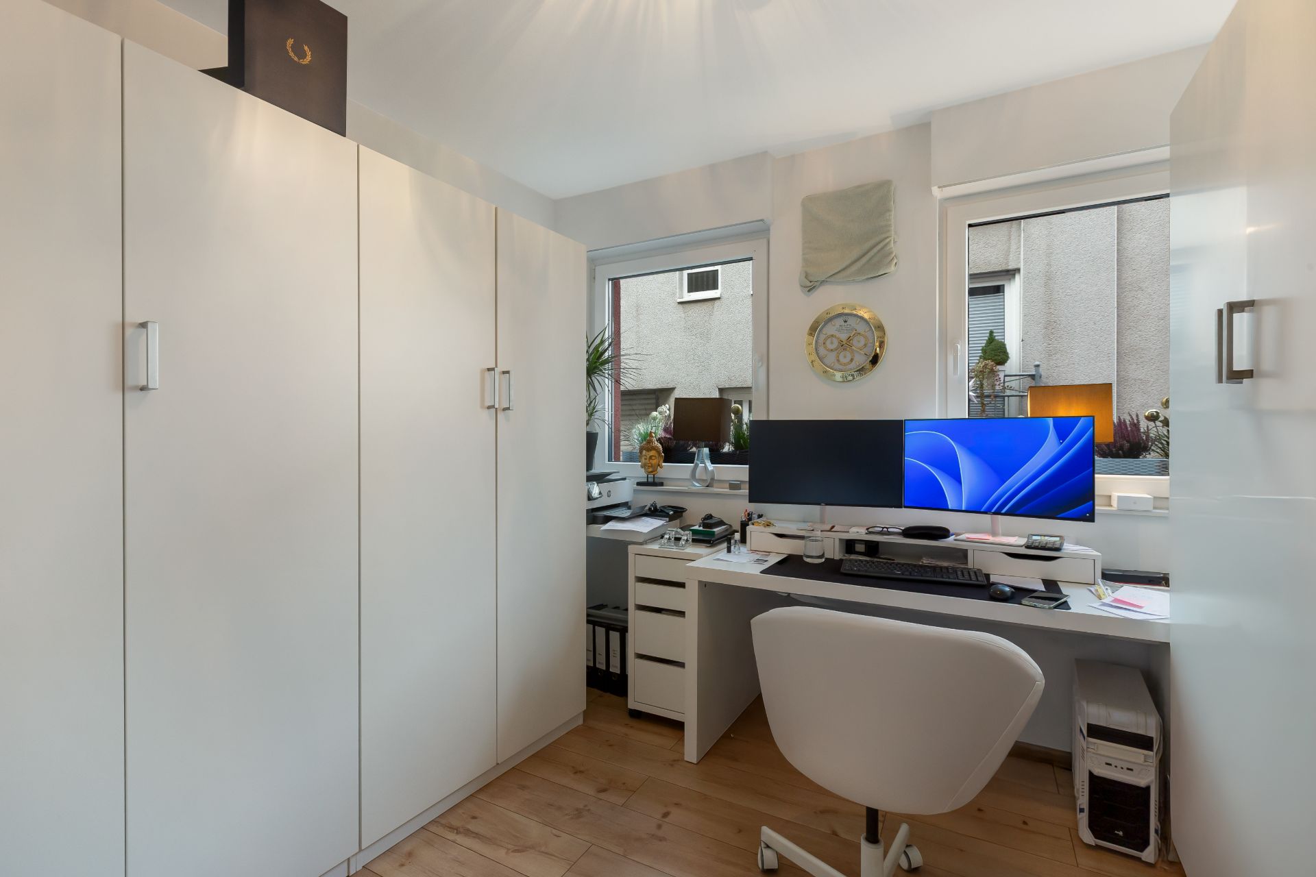 Modernes Arbeitszimmer mit Schreibtisch, zwei Monitoren, weißem Stuhl und Schränken.