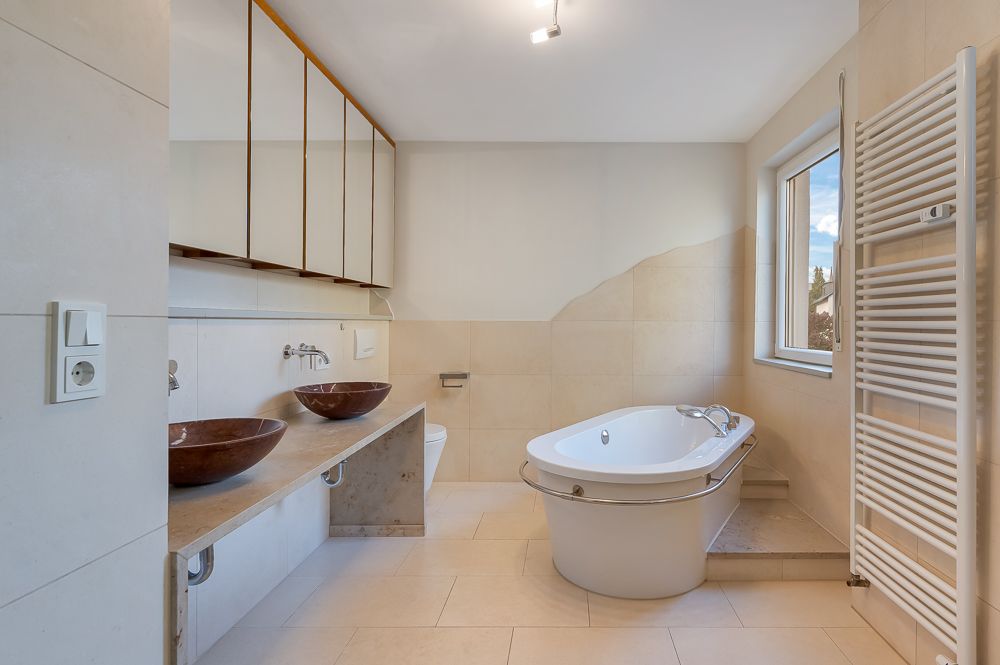Modernes Badezimmer mit Badewanne, Doppelwaschbecken, Spiegeln und Fenster.