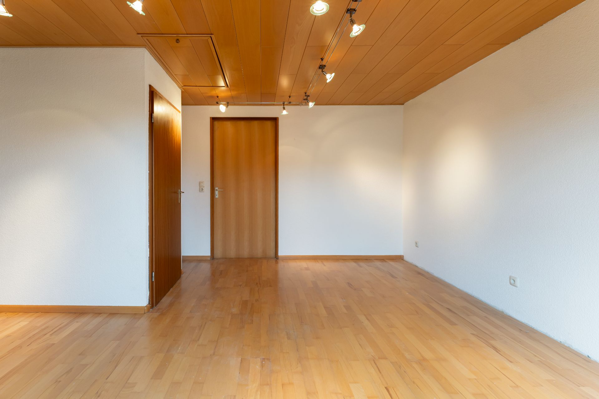 Leerer Raum mit Holzboden, Holztüren und Deckenbeleuchtung.