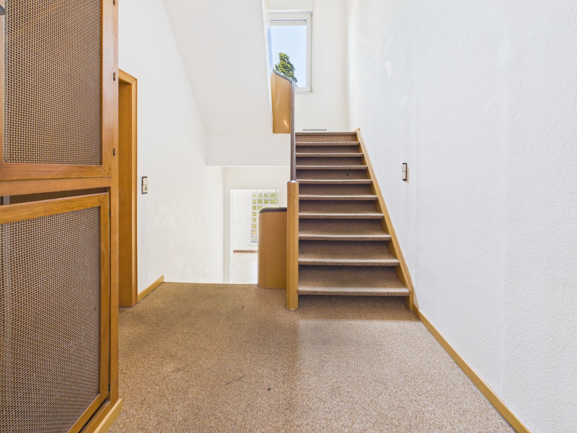 Heller Hausflur mit brauner Treppe und Fenster am oberen Ende.