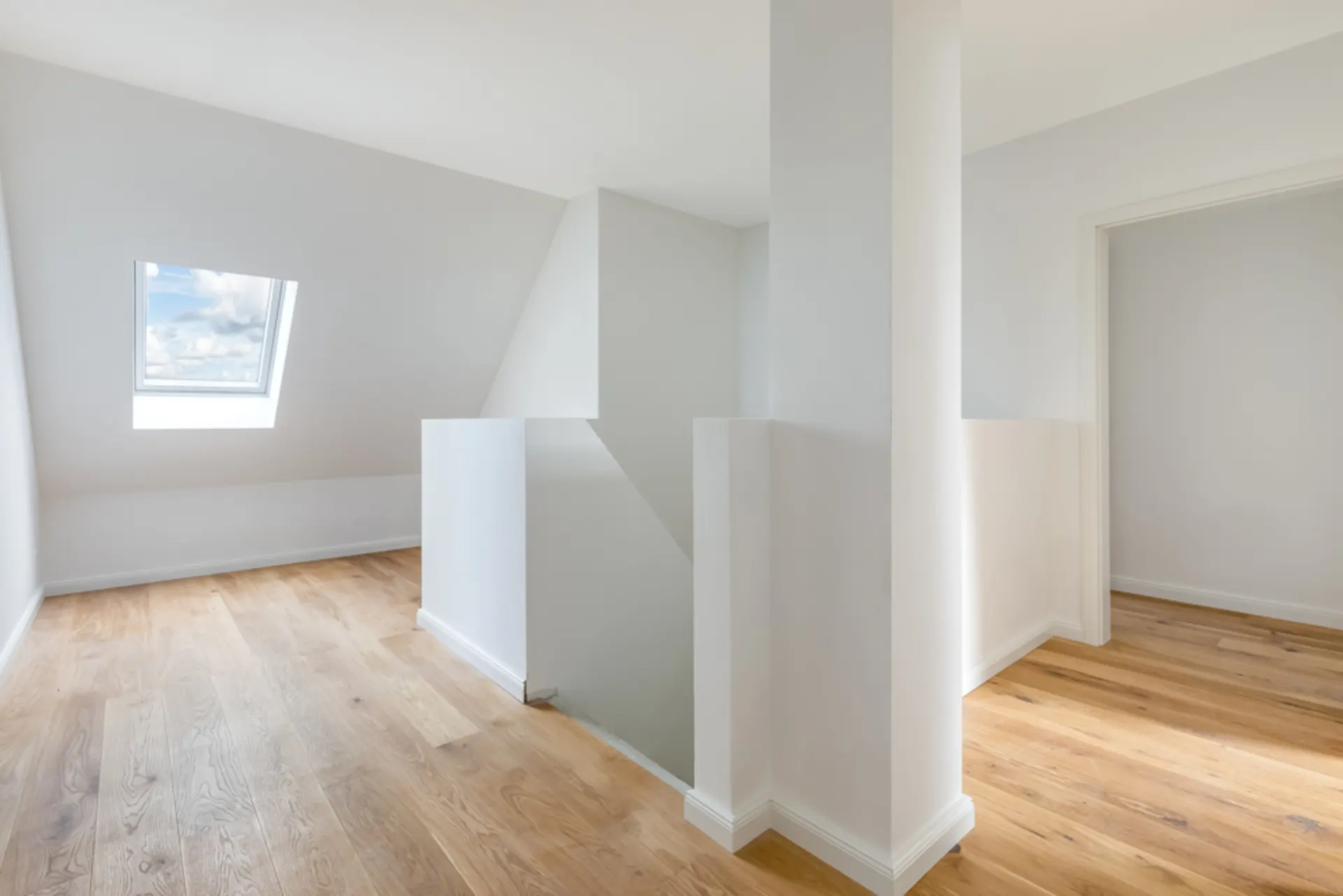 Heller Flur mit Dachfenster, Holzfußboden und Treppenabgang.