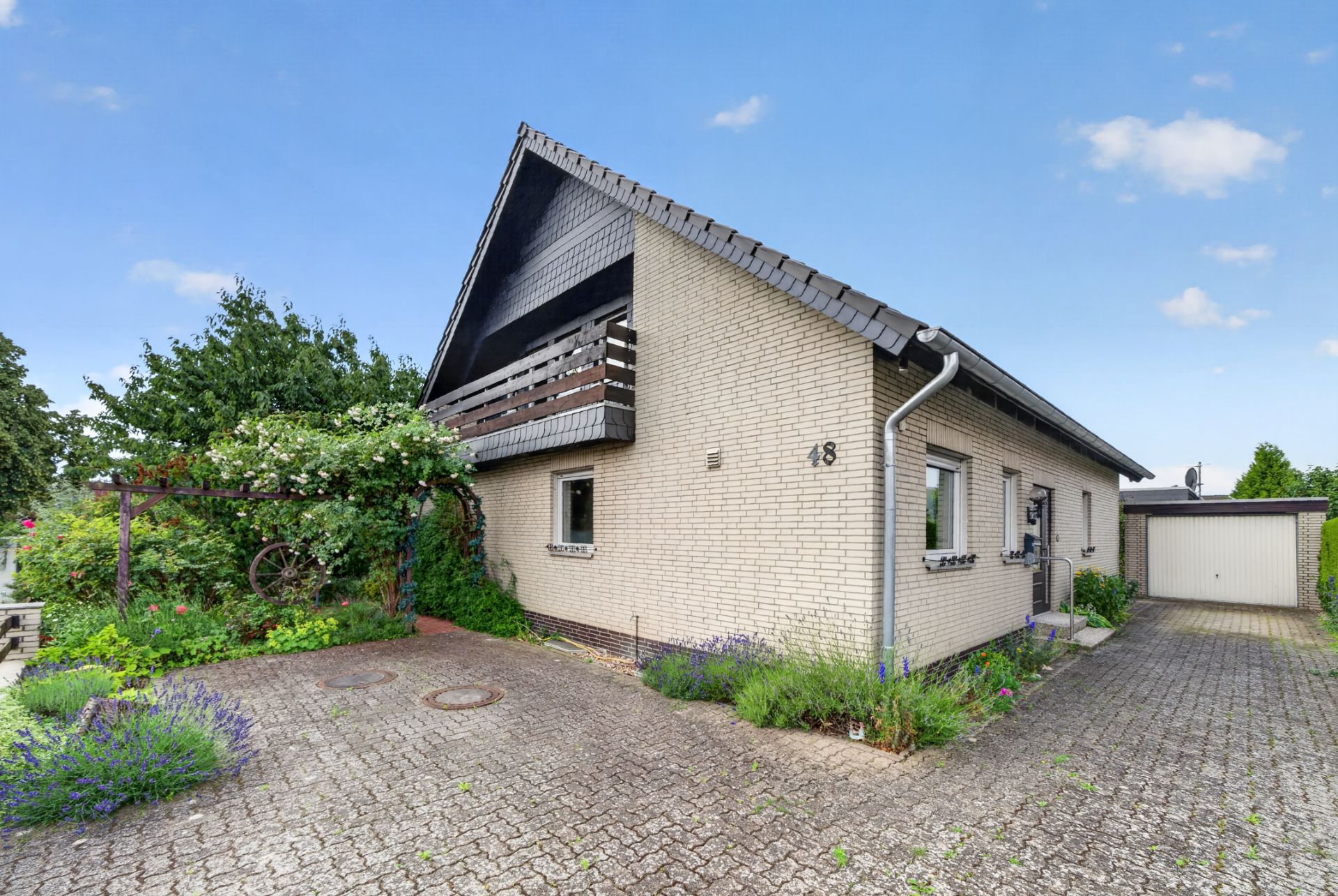 Einfamilienhaus mit Satteldach, Vorgarten und Einfahrt, umgeben von Pflanzen.