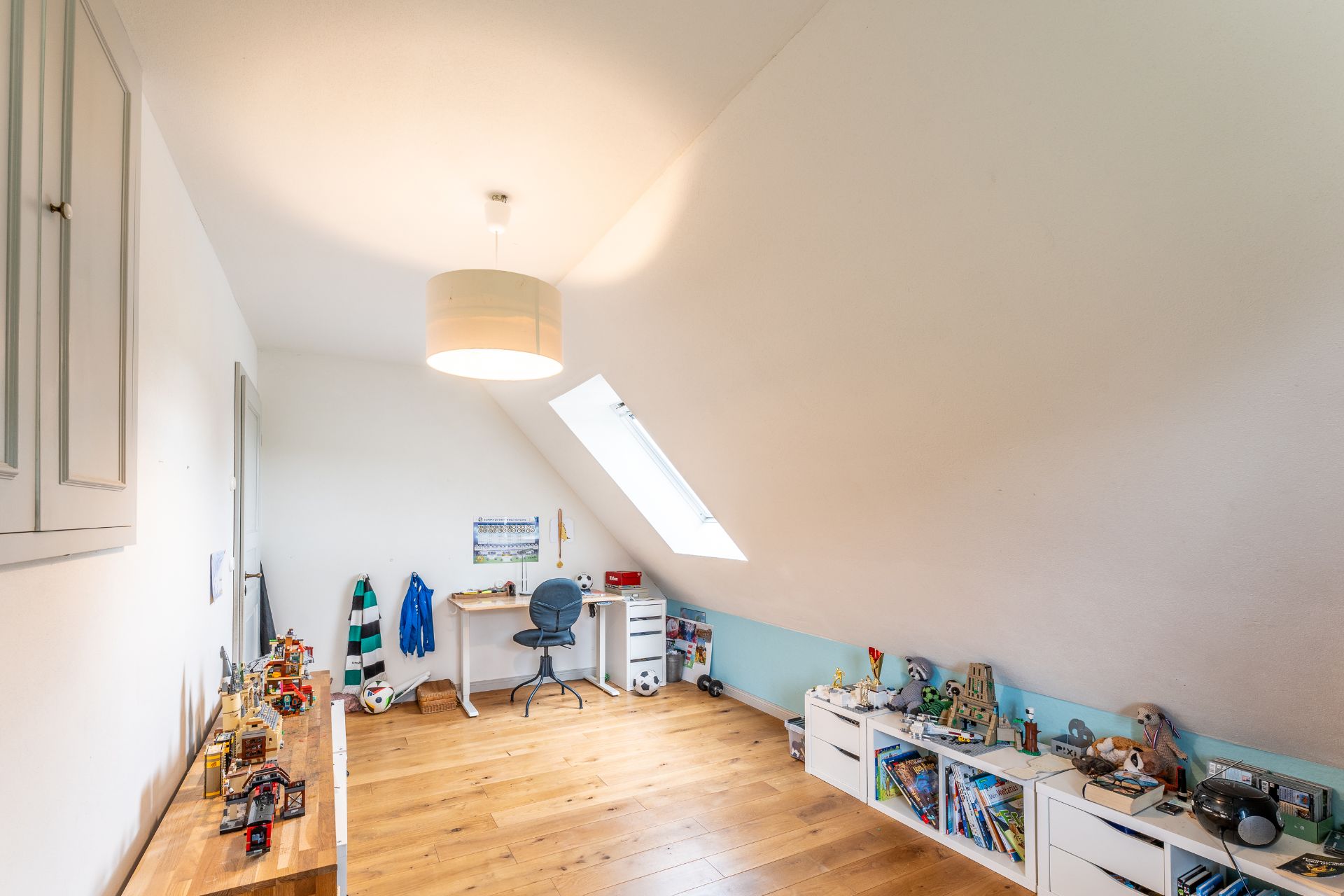 Ein Kinderzimmer mit Schreibtisch, Spielzeugregalen, Dachfenster und Holzfußboden.
