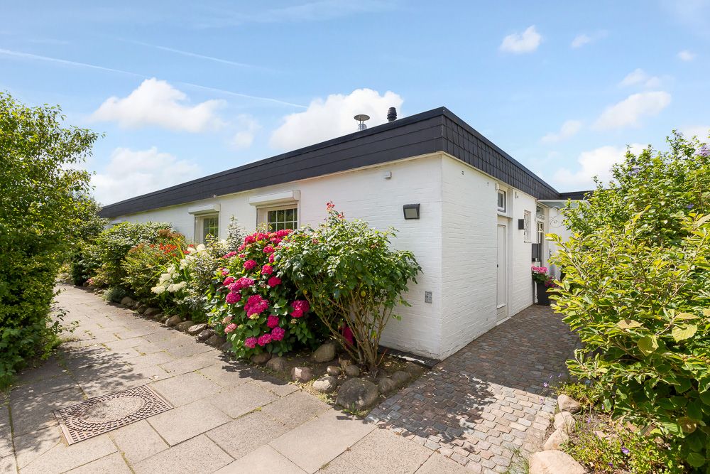 Weißes einstöckiges Haus mit Garten und Blumen an einem Gehweg.