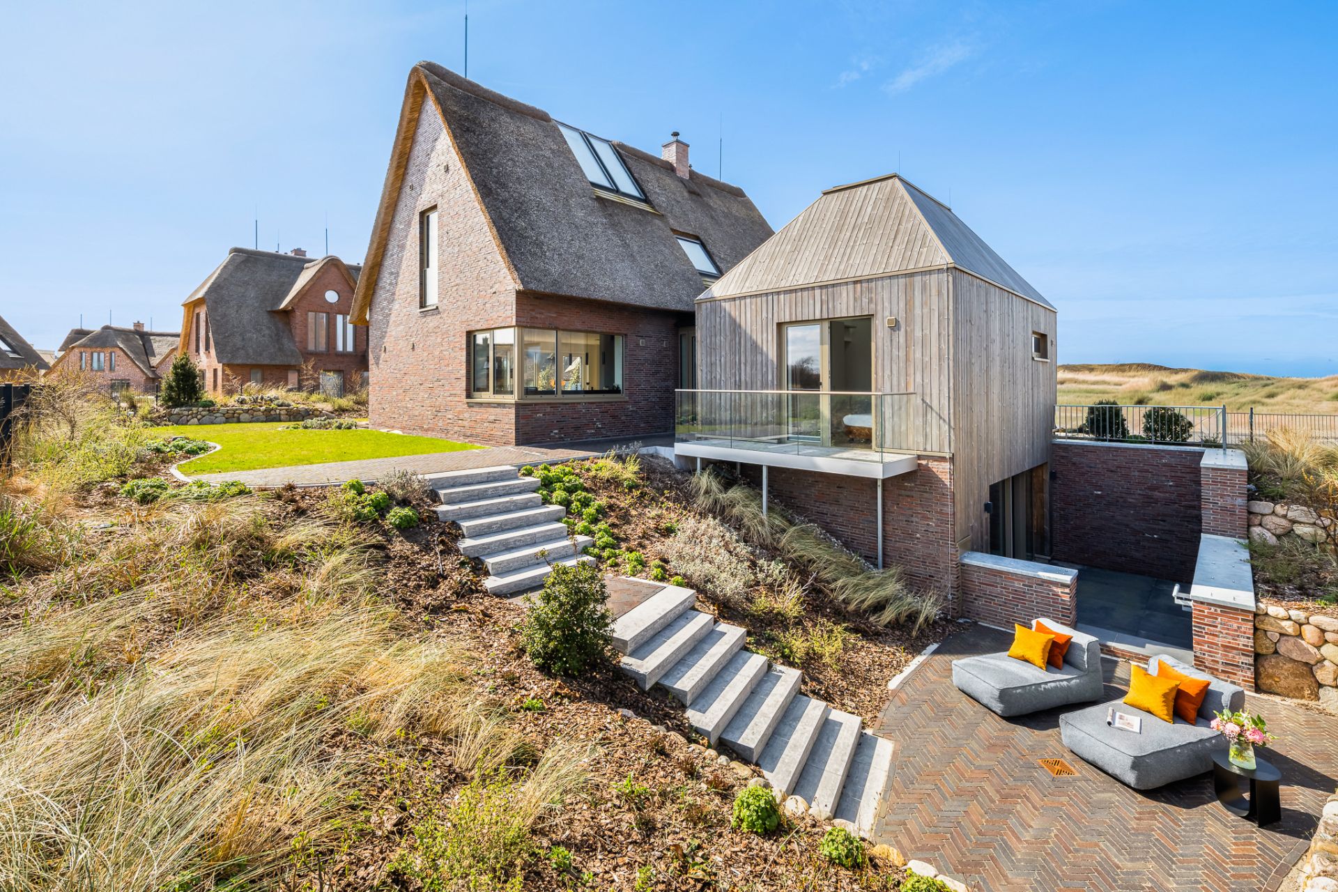 Modernes Haus mit Ziegeldach, Terrasse, Treppen und Sitzbereich im Garten.