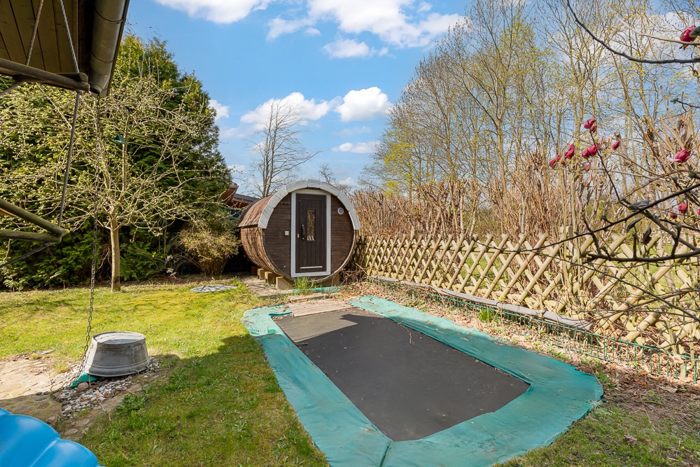 Garten mit eingelassenem Trampolin und einer runden Holzsauna im Hintergrund.