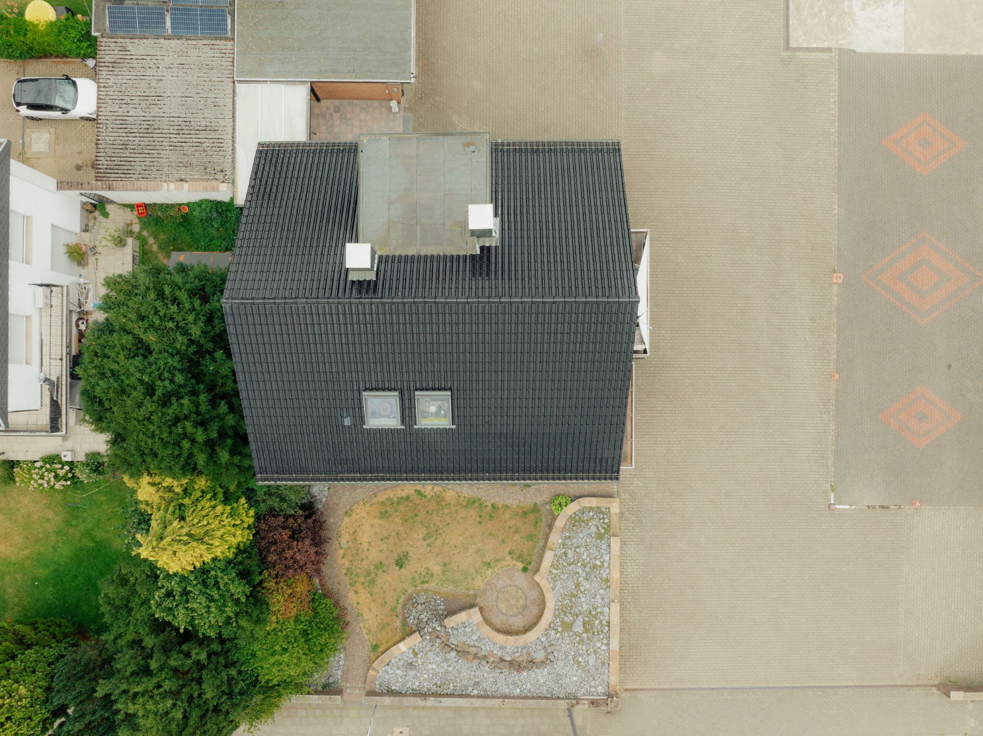 Draufsicht auf ein Haus mit schwarzem Dach und kleinem Garten vor dem Gebäude.