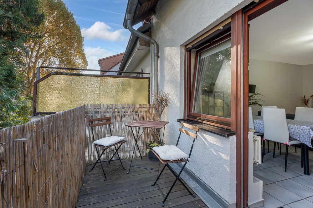 Kleiner Balkon mit zwei Stühlen und einem Tisch, angrenzend an ein Esszimmer mit weißen Stühlen.
