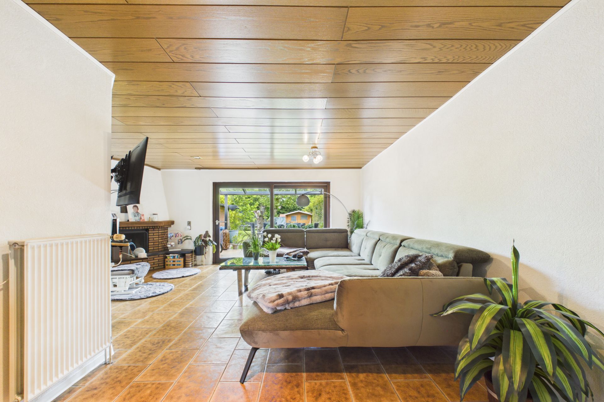 Geräumiges Wohnzimmer mit Ecksofa, Couchtisch, Pflanze und Blick auf den Garten durch große Fenster.