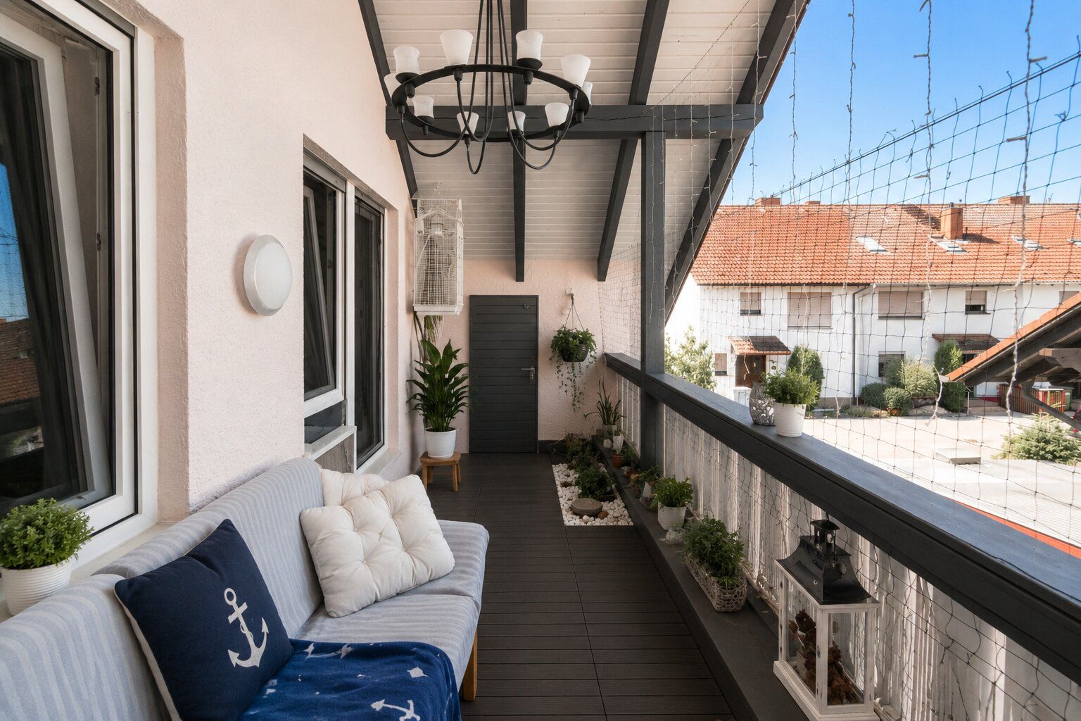 Überdachter Balkon mit Sofa, Pflanzen und Blick auf Wohnhäuser.