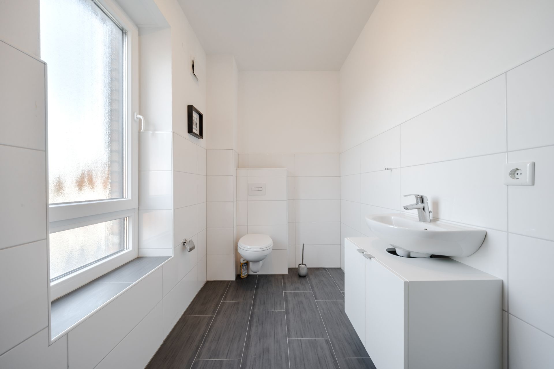 Modernes, helles Badezimmer mit Fenster, Wandtoilette und Waschbecken auf Unterschrank.
