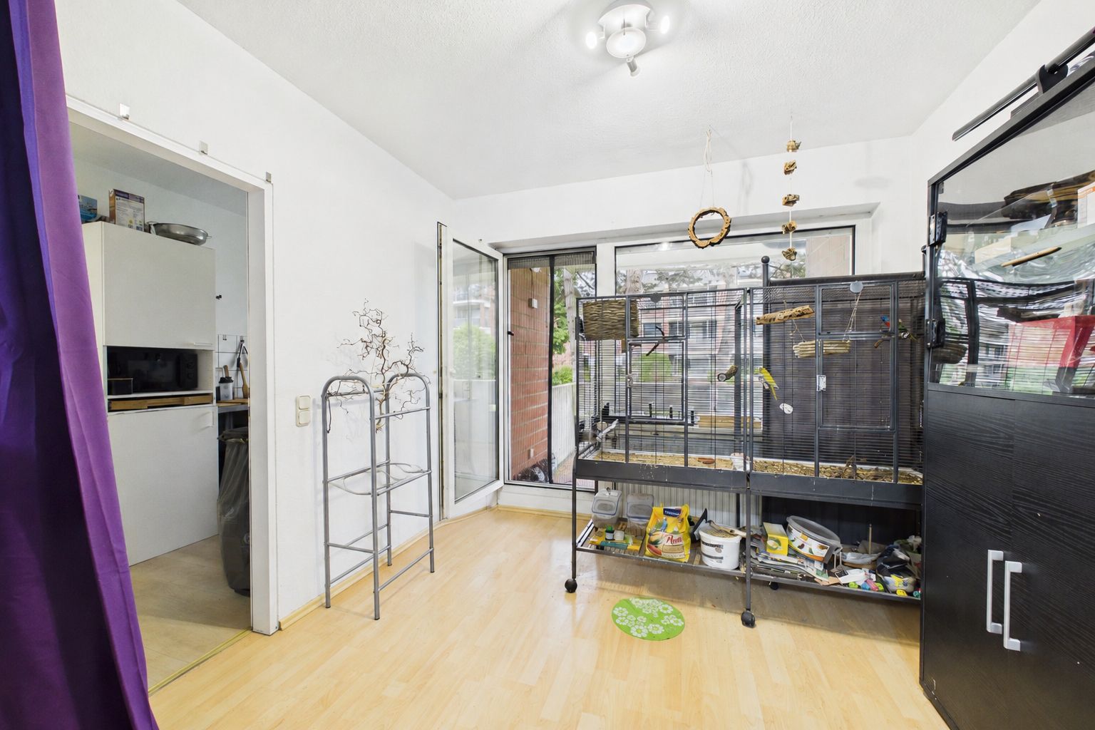 Helles Zimmer mit großem Vogelkäfig, Holzfußboden und Zugang zum Balkon.