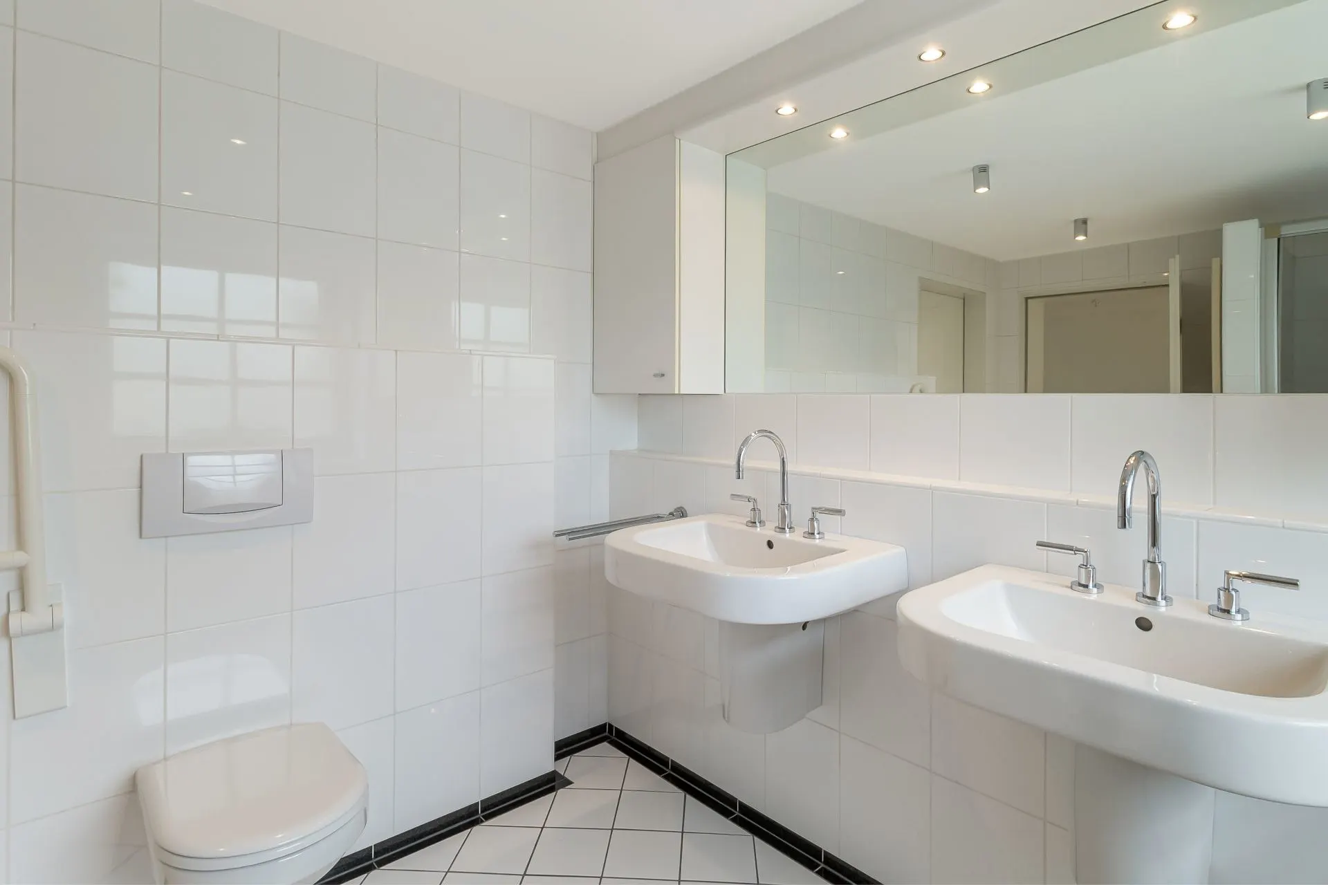Helles Badezimmer mit zwei Waschbecken, großem Spiegel und wandhängender Toilette.